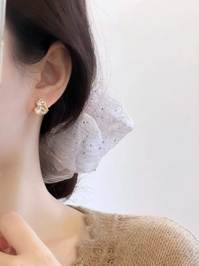 Close-up of golden gourd stud earring with zircon inlay worn by model in soft lighting