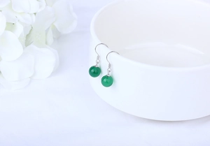 Detail of green agate bead earrings hanging on a white porcelain bowl with flowers