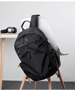 Minimalist black backpack hanging on a white chair with desk accessories in background