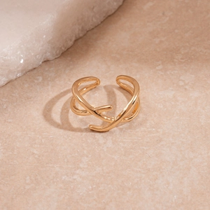Close-up of golden geometric X-shaped cross open ring on beige stone texture surface