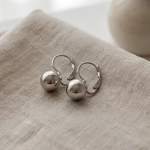 Detailed close-up of silver minimalist steel ball earrings with secure lever-back hooks