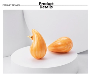 Macro detail of orange marble resin teardrop earrings on a white geometric display