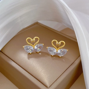 Macro shot of gold swan earrings with clear zircons in a brown jewelry box on silk fabric