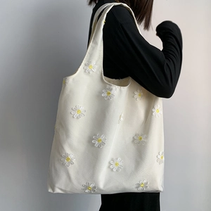 Detail of white canvas tote bag featuring embroidered daisy patterns worn by a model