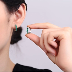 Close-up of minimalist silver hoop earrings featuring sparkling green zircon stones