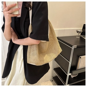 Beige woven mesh tote bag with white shoulder strap on model in a modern interior setting