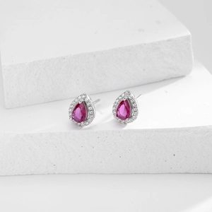 Macro detail of teardrop earrings with rose red stones and halo crystals on white stone