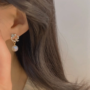 Close-up of golden earrings with moonstone and pearl pendant worn by a model