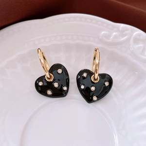 Macro detail of black enamel heart earrings with sparkling diamonds on a ceramic plate