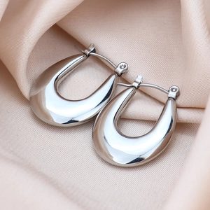 Macro shot of silver U-shaped titanium steel earrings on elegant silk fabric background