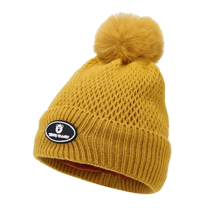 Detail of yellow knit beanie with soft pompom and Teddy Island bear logo badge