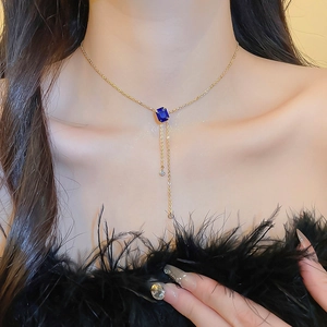 Detail of gold fringe necklace with navy blue rectangular stone and rhinestones on model