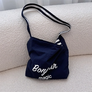 Detail of navy nylon shoulder bag featuring white Bonjour Magic print and striped strap