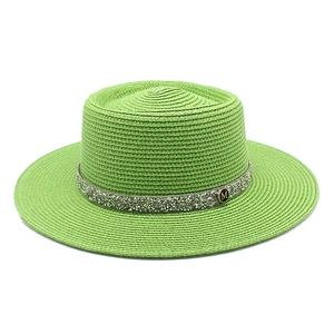 Close-up of green straw boater hat featuring a shimmering sequin band and a metal M charm