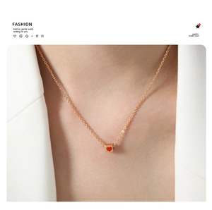 Close-up of gold square pendant with red heart on a delicate chain worn with a white blazer
