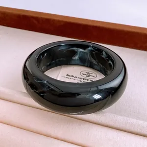 Chic black resin cuff bracelet with white marble patterns on a textured fabric backdrop