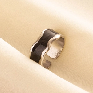 Close-up of wavy 304 stainless steel ring with black enamel oil drip finish on beige fabric