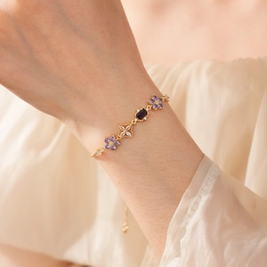 Detail of adjustable gold bracelet featuring purple flower zircons on a model's wrist