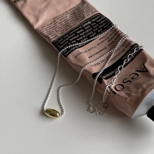 Detail of 925 sterling silver bead chain with minimalist golden olive pendant on cream tube