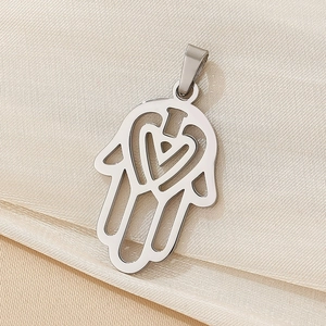 Macro shot of silver Hamsa Hand pendant with hollow heart pattern on satin cloth