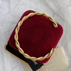 Macro detail of gold C-shape twisted rope cuff bracelet on red velvet cushion