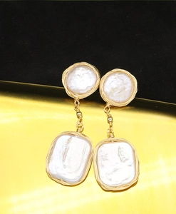 Detailed view of long gold earrings with baroque pearls and rectangular golden pendants
