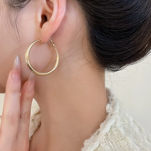 Close-up of elegant large golden hoop earrings on model with high gloss finish