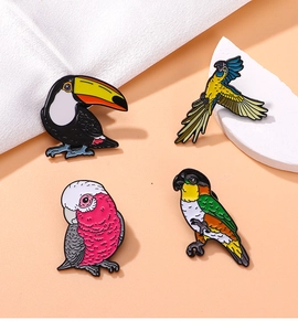 Flat lay of colorful enamel bird pins including toucan and macaw on beige background