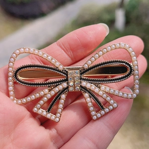 Elegant gold bow hair clip with pearls and rhinestones held by hand in natural light