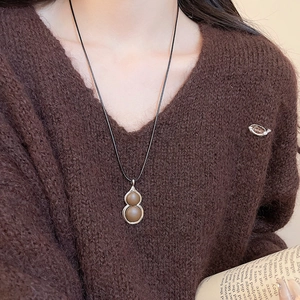 Detail of a brown gourd pendant with silver metal frame on a long black sweater chain