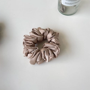 Macro detail of champagne gold satin scrunchie with elegant pleated fabric texture