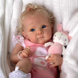 Lifelike 18-inch reborn baby doll in pink bunny onesie lying on soft white plush background