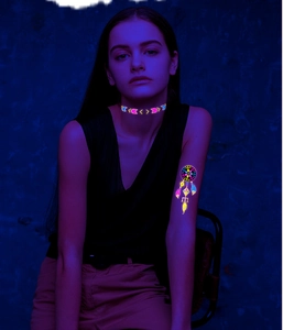 Close-up of glowing fluorescent tattoo stickers on neck and arm in dark blue light
