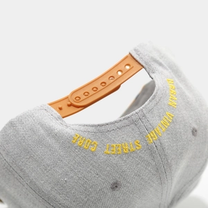 Detail of adjustable orange plastic strap and yellow embroidery on a gray flat-brim hat