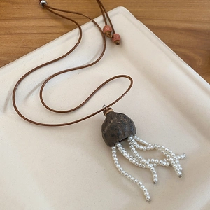 Macro detail of Zen style necklace with ceramic bell pendant and pearl tassels on a tray