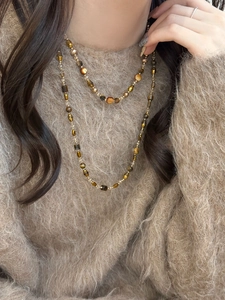 Détail du collier de perles en oeil de tigre multicouche sur un pull marron au style rétro