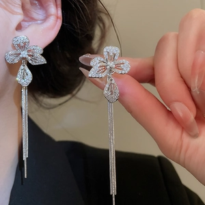 Macro detail of silver flower earrings with long zirconia tassels and a white pearl accent