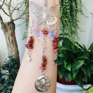 Detail of silver suncatcher with butterfly and moon pendants against green plants