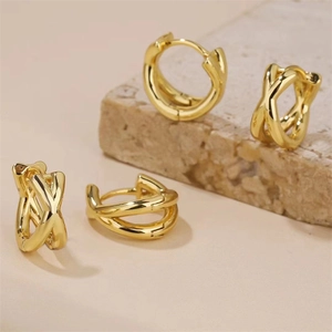 Vue détaillée des boucles d'oreilles dorées croisées au design géométrique sur pierre beige