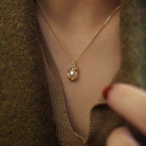 Close-up of a teardrop baroque pearl pendant on a gold chain worn on a knit sweater