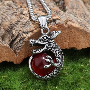 Detailed shot of silver dragon pendant holding a red bead on a rustic tree bark