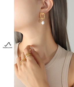 Detail of 18K gold plated stainless steel pearl drop earrings and stacked rings