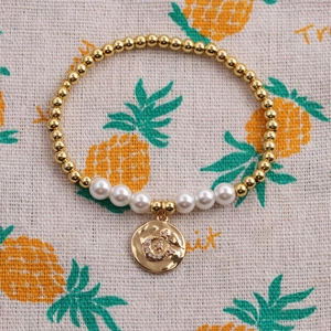 Bracelet doré avec pendentif lune étoile et perles blanches sur fond texturé rustique