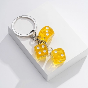 Detail of three yellow transparent dice charms on a silver metal keychain with a white background