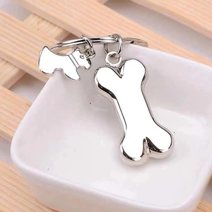 Silver metal keychain with puppy and bone pendants in a white ceramic bowl