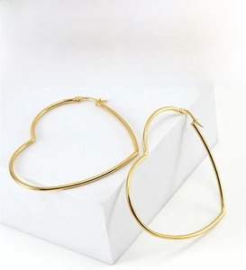 Detailed close-up of large golden heart-shaped hoop earrings with polished steel finish