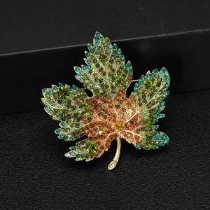 Detailed close-up of maple leaf brooch with green, blue, and orange gradient crystals