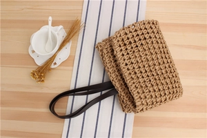 Detail of handwoven straw bag texture with dark brown leather strap on wooden table