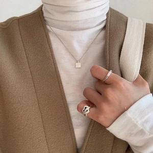 Detailed view of square pendant necklace and rings on beige wool vest outfit