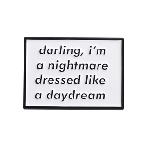 Modern white enamel brooch with black text 'darling, i'm a nightmare dressed like a daydream'